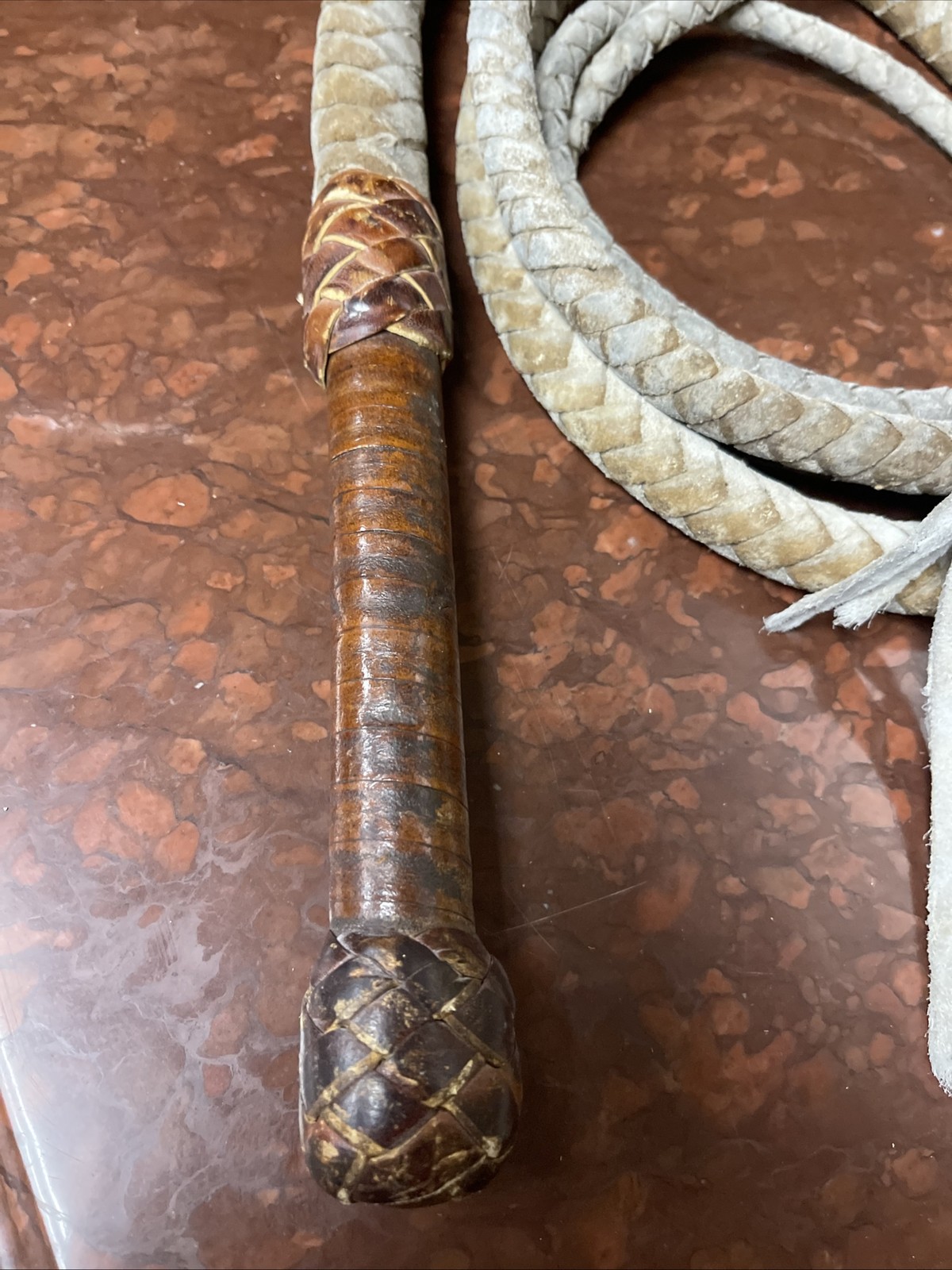 Vintage braided leather bullwhip with a patterned handle.
