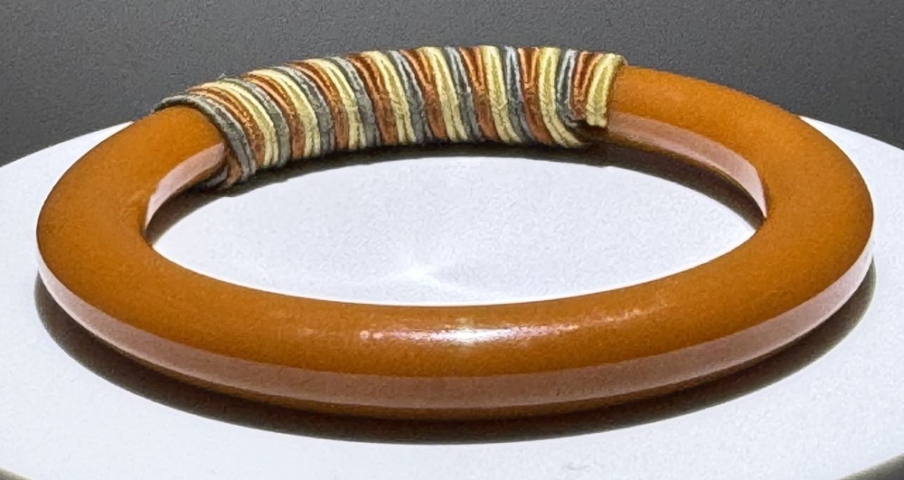 Red/white/blue string-wrapped, rust-colored Bakelite bracelet; tested
