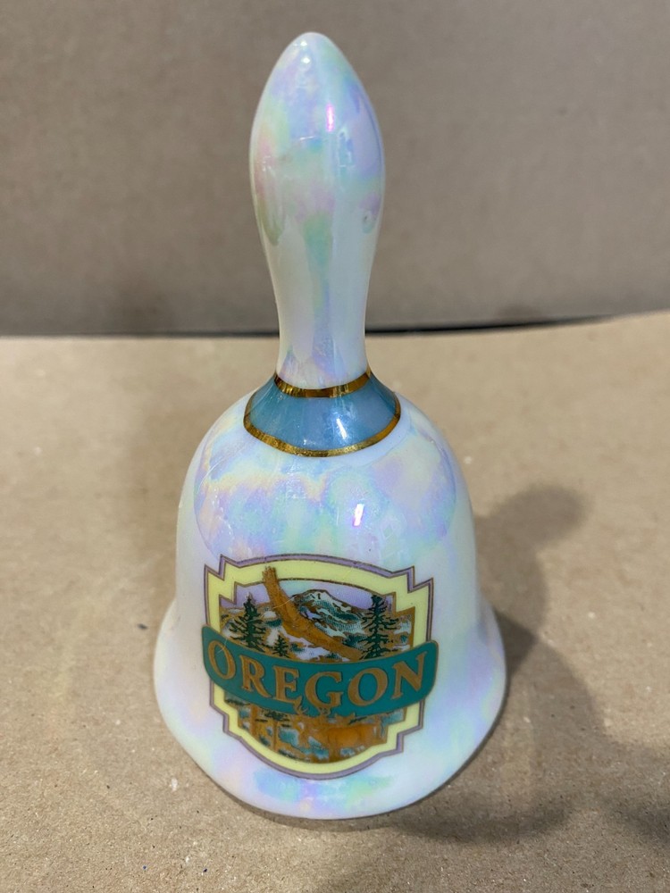 Ceramic bell from Oregon, white pearl background with green forestry.