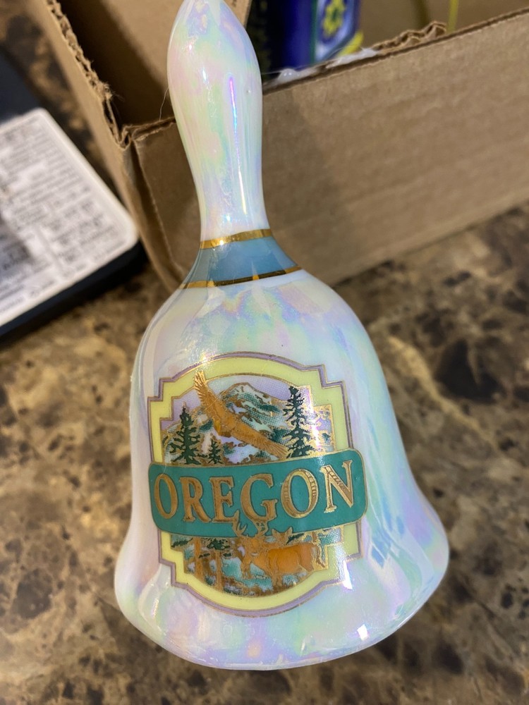 Ceramic bell from Oregon, white pearl background with green forestry.
