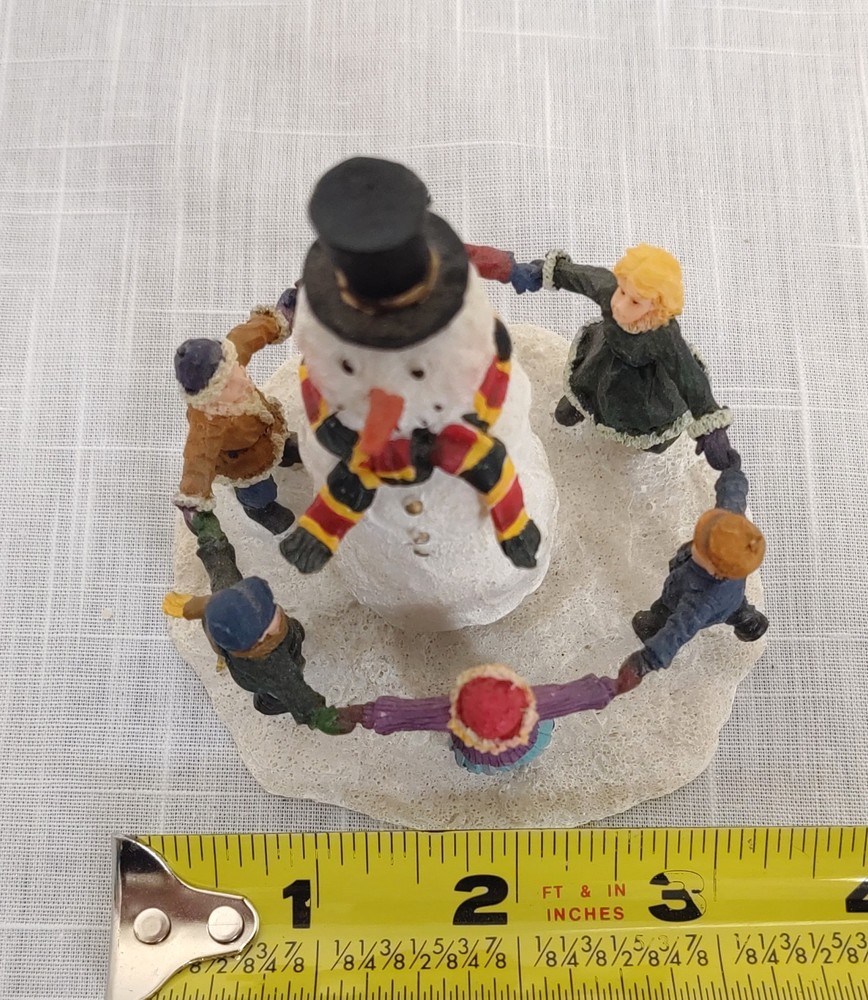 CHILDREN DANCING AROUND A SNOWMAN FIGURINE