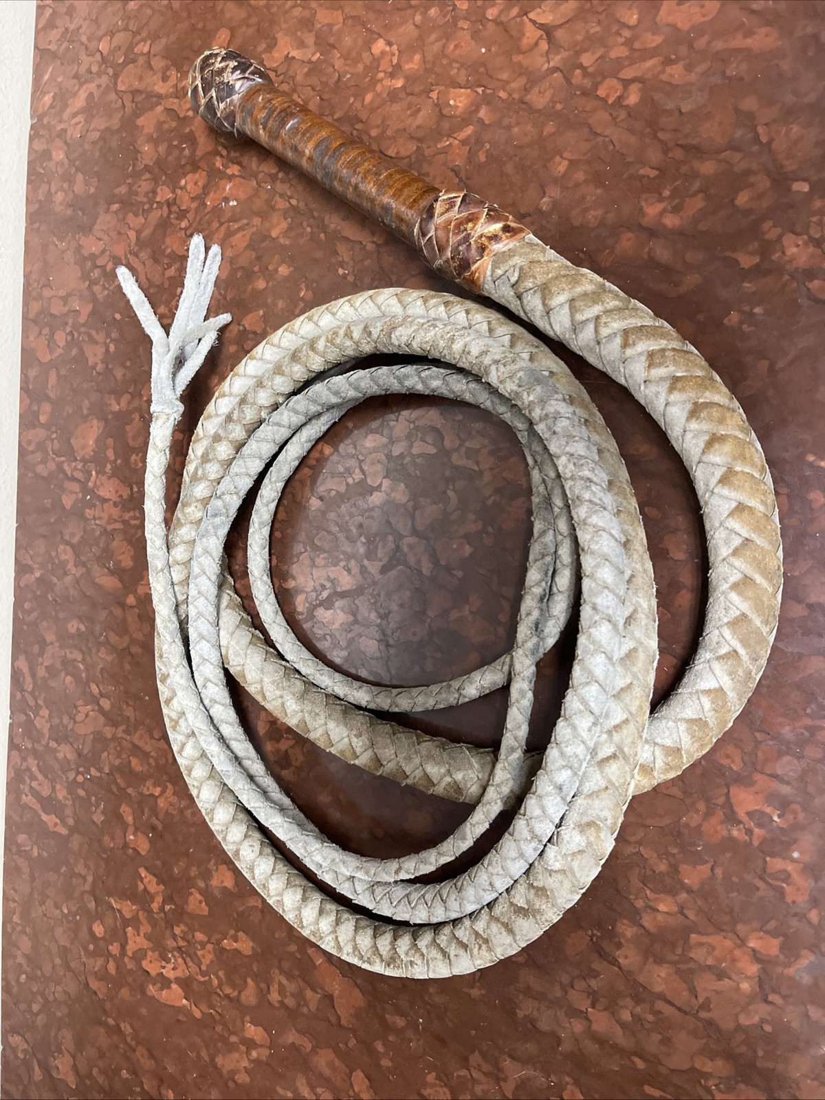 Vintage braided leather bullwhip with a patterned handle.