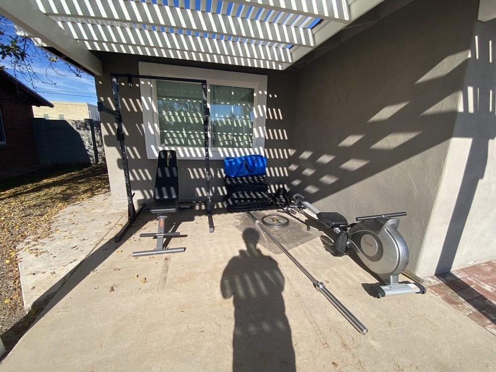 Squat Rack With Bench, Weights, Two Barbells, And A Rowing Machine