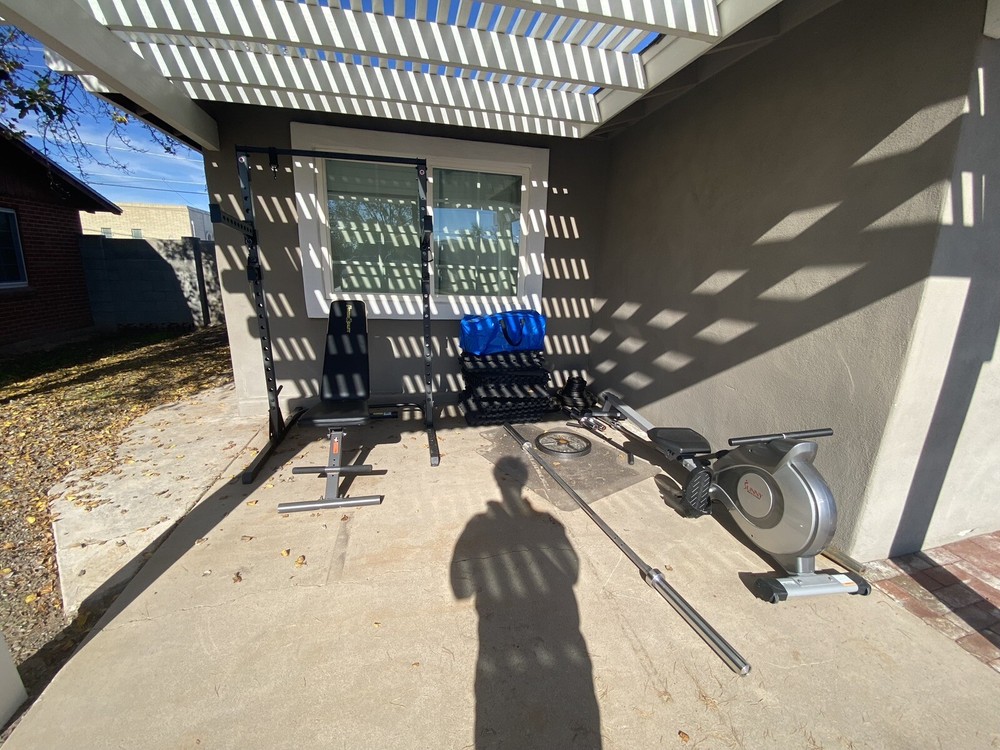 Squat Rack With Bench, Weights, Two Barbells, And A Rowing Machine